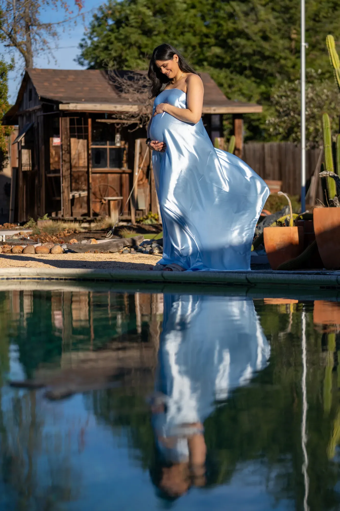 Maternity shoot in a flowing blue dress reflected in a pool