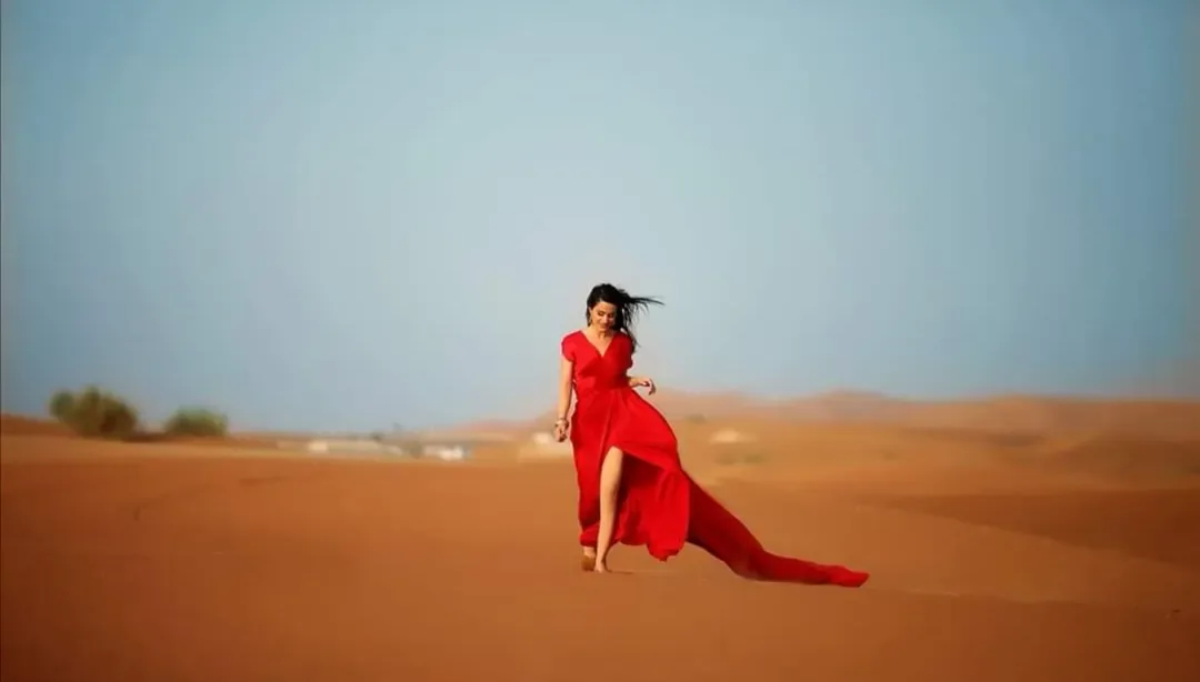 Woman in a flowing red dress on desert sand dunes