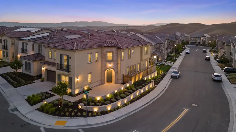 Aerial drone photo of a Mediterranean-style home at twilight with landscape lighting