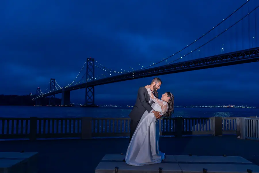 Couple dancing at night with the Bay Bridge lit up behind them