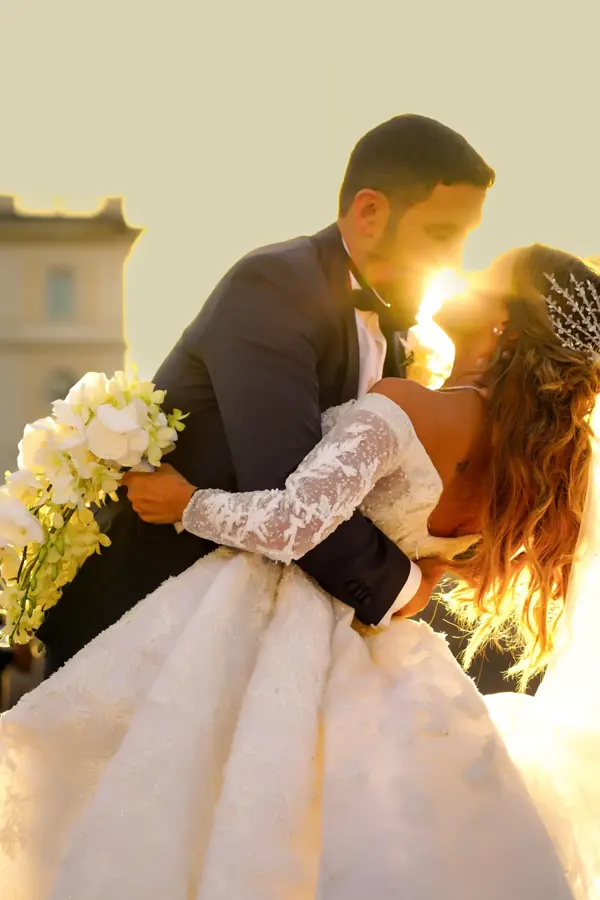 Groom kissing the bride in warm backlight holding white orchids
