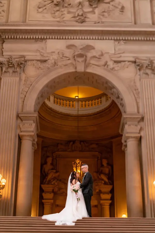 Bride and groom on grand marble stairs under an arch, San Francisco City Hall