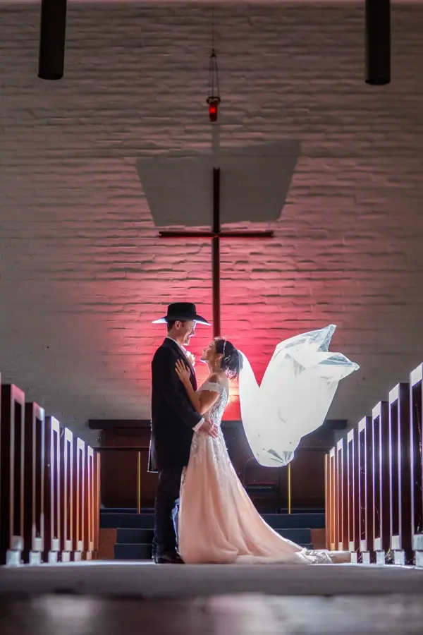 Couple in a chapel aisle with the veil floating and a cross behind them