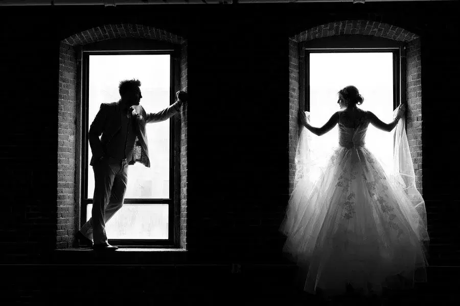 Silhouettes of the bride and groom in two tall windows, black and white